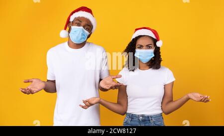 Couple noir portant des masques coronavirus et des chapeaux de Noël, fond jaune Banque D'Images