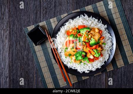 Poulet à la noix de cajou thaï aux légumes sautés : brocoli, poivron, piment rouge chaud et sauce soja servis sur une assiette noire avec du riz et des baguettes Banque D'Images