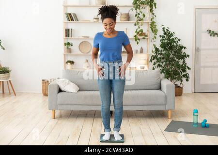 Femme africaine souriante se pesant sur des balances posant à la maison Banque D'Images