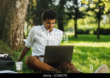 Un étudiant souriant avec un ordinateur portable sur les hanches est assis le parc Banque D'Images