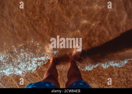 Mans pieds dans l'eau claire on beach Banque D'Images