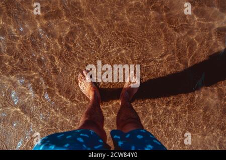 Mans pieds dans l'eau claire on beach Banque D'Images