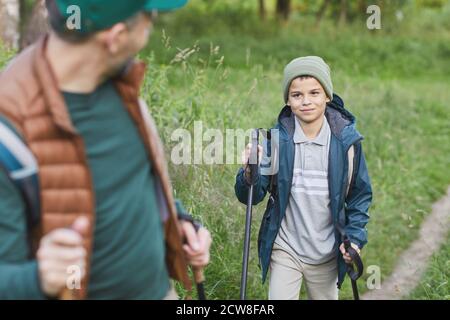 Portrait d'un père heureux et d'un fils qui marchent ensemble et qui monte en montée, se concentre sur un garçon souriant avec des bâtons de randonnée, espace de copie Banque D'Images