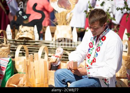 08 29 2020 Bélarus, Lyakhovichi. Vacances en ville. Un homme bélarussien dans une chemise brodée fabrique des produits à partir d'écorce de bouleau. Banque D'Images