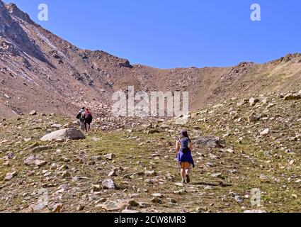 Groupe de touristes se déplaçant le long d'un chemin dans les montagnes rocheuses avec l'herbe vers le col; concept de mode de vie actif Banque D'Images