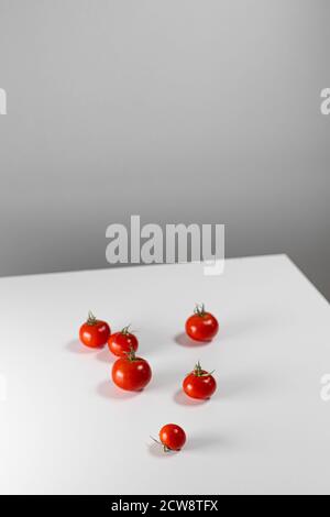 Beaucoup de tomates cerises fraîches sur une table blanche. Concept de composition géométrique tendance et créatif. Orientation verticale de la photo Banque D'Images