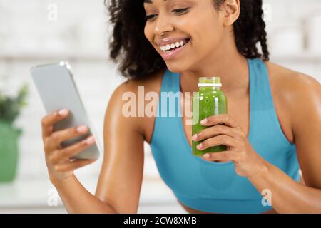 Black Lady Drinking Smoothie et en utilisant le téléphone cellulaire Banque D'Images