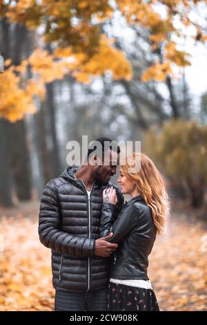 Heureux mignon couple interracial posant dans le parc d'automne flou, homme noir et femme rouge blanc Banque D'Images