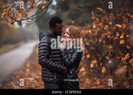 Heureux mignon couple interracial posant dans le parc d'automne flou, homme noir et femme rouge blanc Banque D'Images