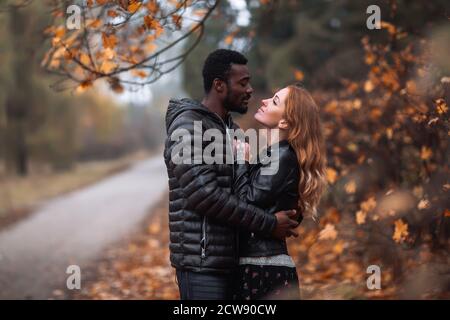 Heureux mignon couple interracial posant dans le parc d'automne flou, homme noir et femme rouge blanc Banque D'Images