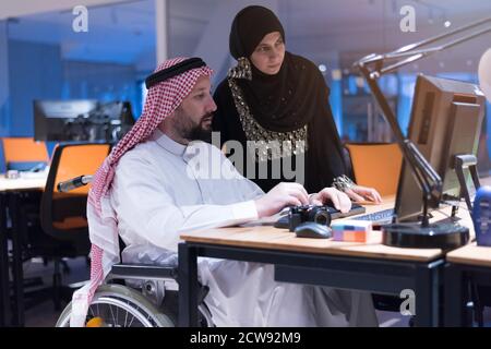 Un homme d'affaires arabe handicapé dans la tradition s'adapte avec une femme arabe assiposante travaillant au bureau. Homme d'affaires handicapés dans le fauteuil roulant travaille dans l'o Banque D'Images