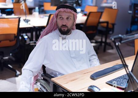 Homme d'affaires arabe handicapé dans la tradition costume travaillant dans le bureau. Homme d'affaires handicapé dans le fauteuil roulant travaille dans le bureau à l'ordinateur. Banque D'Images