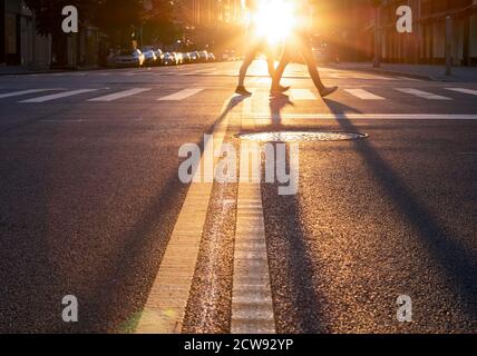 Homme et femme marchant de l'autre côté de la rue à New York Ville avec la lumière du coucher de soleil jetant de longues ombres de leurs jambes Banque D'Images