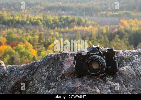 Un appareil photo analogique Olympus OM-1n pour le format de film 35 mm se trouve à l'extérieur, au-dessus d'une falaise, en Ontario, au Canada, avec une forêt mixte derrière lui au début Banque D'Images