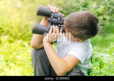 curieux garçon cherche la faune à travers des jumelles dans le parc. Exploration du monde, observation des oiseaux. Activités de plein air. Garçon regardant loin dans la dista Banque D'Images