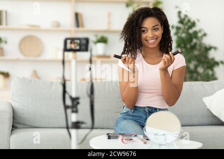 African American Female Beauty Blogger examinant les cosmétiques assis à la maison Banque D'Images