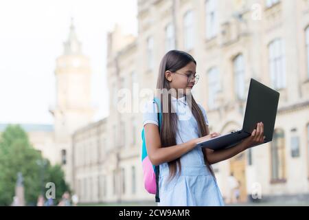 une jeune fille intelligente travaille sur un ordinateur portable en ligne dans la cour de l'école, l'éducation et le développement de l'enfance. Banque D'Images