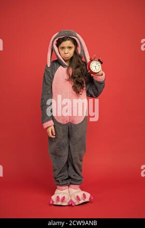 Jour normal de début. Adorable réveil à motif lapin. Petite fille en costume de lapin. Enfant lapin kigurumi. Pyjama fille à motif lapin. Bunny rouge enfant fond. Bébé animal. Temps de comptage. Alarme du matin. Banque D'Images