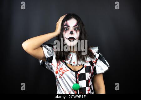 femme dans un costume de clown d'halloween sur fond noir isolé mettre une main sur sa tête en souriant comme elle l'avait fait quelque chose oublié Banque D'Images