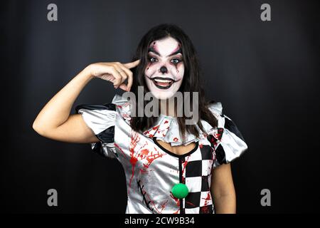 femme dans un costume de clown d'halloween sur fond noir isolé souriant et pensant avec ses doigts sur sa tête qu'elle a une idée. Banque D'Images