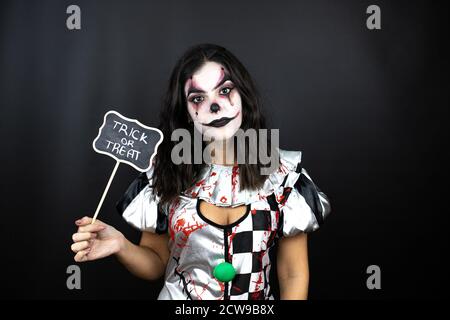 femme dans un costume de clown d'halloween sur fond noir isolé tenir le tableau noir avec le mot trick ou traiter le message Banque D'Images