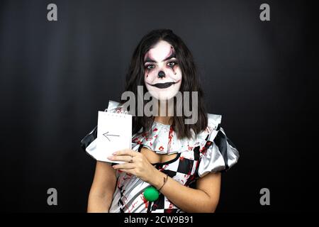 femme dans un costume de clown d'halloween sur fond noir isolé tenir le bloc-notes avec le message fléché Banque D'Images