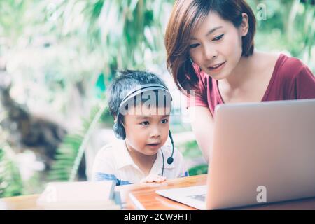 Jeune mère asiatique et son fils utilisant un ordinateur portable pour étudier et apprendre ensemble à la maison, garçon portant un casque pour l'e-learning avec distanciation, teatie Banque D'Images