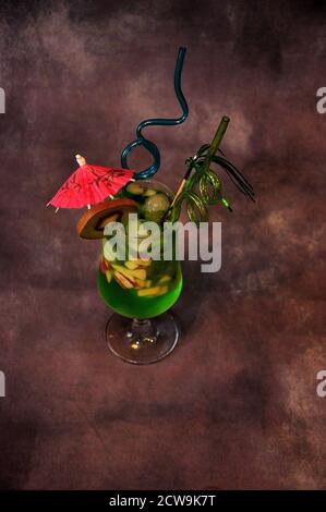Un verre de jus à base de kiwi avec glace, morceaux de fruits, parapluie et pailles. Gros plan. Banque D'Images