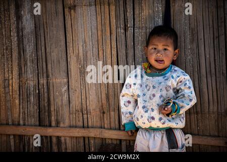 Chiang Mai / Thaïlande - 16 janv. 2016: Garçon de corps déchiqueté portant des vêtements vieux et mauvais, debout sur un mur de bambou tissé dans un village rural dans le nord Banque D'Images