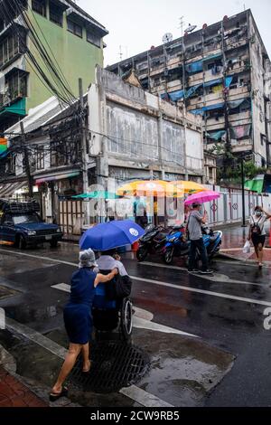 Une femme pousse un homme dans un fauteuil roulant de l'autre côté de la rue vers un vendeur de nourriture dans Chinatown. Banque D'Images