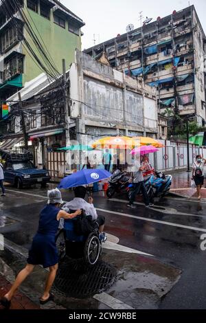 Une femme pousse un homme dans un fauteuil roulant de l'autre côté de la rue vers un vendeur de nourriture dans Chinatown. Banque D'Images