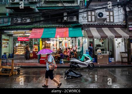 Un homme descend dans la rue avec un petit parapluie violet dans le quartier chinois de Bangkok. Banque D'Images