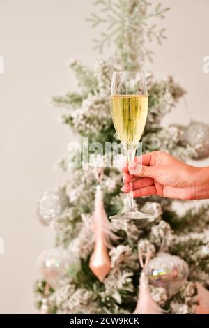 Une main féminine tenant une coupe de champagne avec un arbre de Noël hors foyer et des bonbons traditionnels à l'arrière. Concept de fête de Noël. Banque D'Images