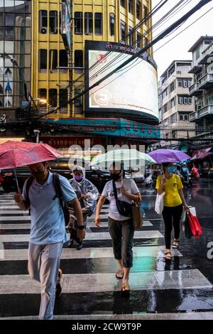 Les employés de bureau se trouvent de l'autre côté d'une rue animée, sous la pluie, en rentrent du quartier chinois de Bangkok. Banque D'Images