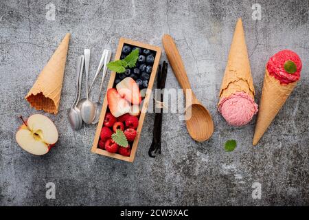 Divers de saveur de crème glacée dans des cônes avec des baies en boîte de bois sur fond de béton . Concept de menu été et sucré. Banque D'Images
