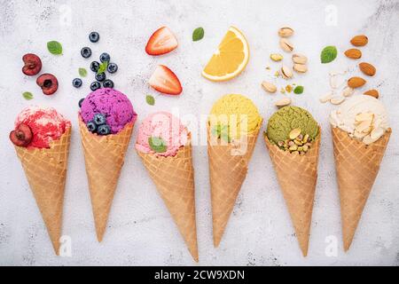 Divers de saveur de crème glacée en cônes bleuet, pistache, amande, orange et cerise sur fond de pierre blanche. Concept de menu été et sucré. Banque D'Images
