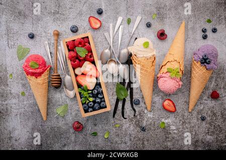 Divers de saveur de crème glacée dans des cônes avec des baies en boîte de bois sur fond de béton . Concept de menu été et sucré. Banque D'Images