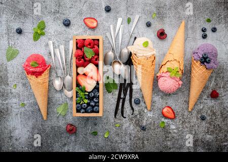 Divers de saveur de crème glacée dans des cônes avec des baies en boîte de bois sur fond de béton . Concept de menu été et sucré. Banque D'Images