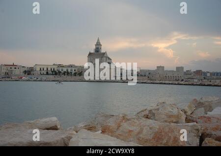 La cathédrale de Trani au bord de la mer et quelques rochers et port en premier plan dans la lumière du soir Banque D'Images