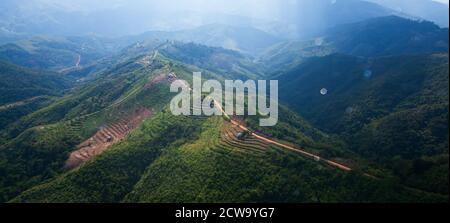 Vue aérienne de la route de terre de montagne et des terrasses de riz en saison de pluie, sunbeam brille à travers le ciel nuageux sur une montagne, scène rurale dans le sud du Myanmar. Banque D'Images