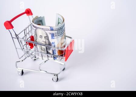 Le panier du supermarché est rempli d'argent. Dollars dans un chariot sur fond blanc. Le concept de shopping. Banque D'Images