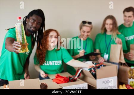 un homme volontaire africain affable donne de l'huile de tournesol pour les hommes pauvres, tout ce dont ils ont besoin, organisation caritative Banque D'Images