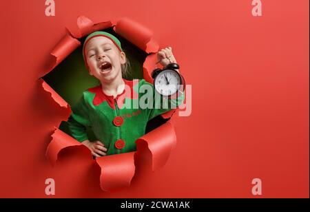 Joyeux Noël ! Petite fille en costume d'orf du Père Noël sur fond de couleur vive. Rouge et vert. Banque D'Images