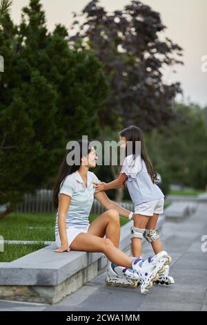 une petite fille heureuse et sa mère portent des patins à roulettes tout en étant assise dans le parc d'été. Banque D'Images