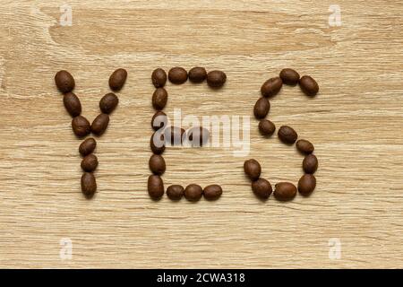 Le mot « Oui » est disposé avec des grains de café arabica torréfiés sur une table en bois. Banque D'Images