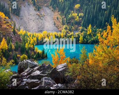 Vue sur le lac de montagne d'Issyk. Le lac turquoise est entouré de montagnes avec des arbres à jaunins. Banque D'Images