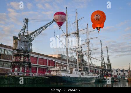 Des ballons passent au-dessus des navires sur le port de Bristol pendant le vol inaugural d'une montgolfière en forme de Wallace and Gromit's Moon Rocket après le lancement depuis l'amphithéâtre Lloyds de Bristol. Banque D'Images