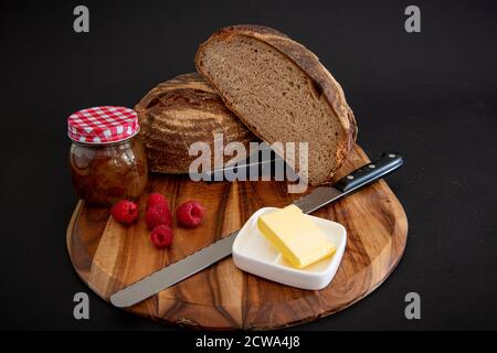 Pain de seigle sur une planche de bois avec beurre et framboises avec un arrière-plan sombre Banque D'Images