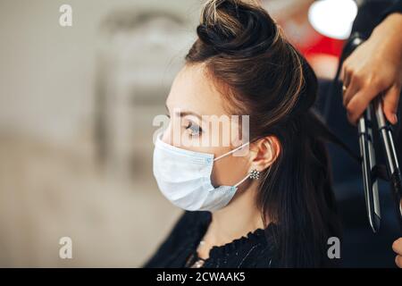 Femme dans le masque médical obtient ses cheveux fait dans la beauté salon pendant une pandémie Banque D'Images