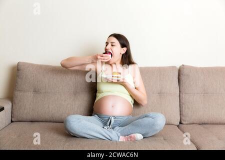 La bonne femme affamée aime manger de délicieux gâteaux se détendre à la maison. Concept de nourriture douce savoureuse pendant la grossesse. Banque D'Images